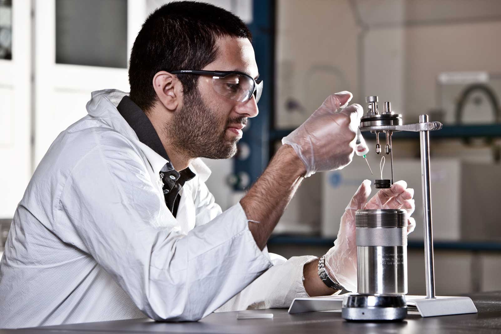 A man with a lab coat with protective eye gear and gloves doing an experiment.