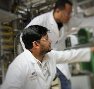 Dr. Hanif in a lab coat and safety glasses working in his lab.
